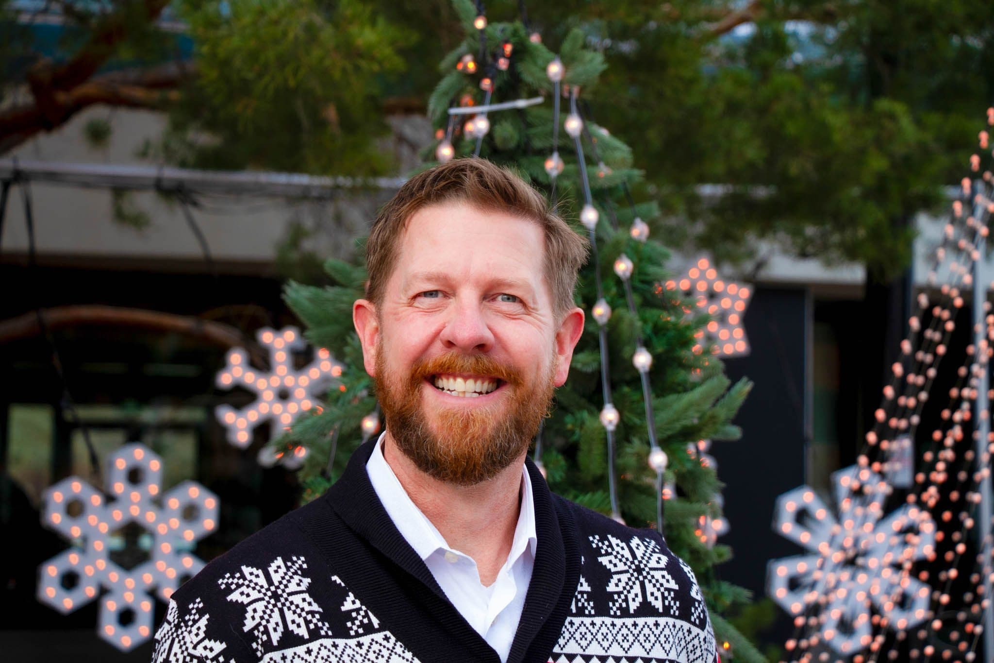 Kyle Kasawski wears a Christmas sweater in front of Christamas trees at Festival Place