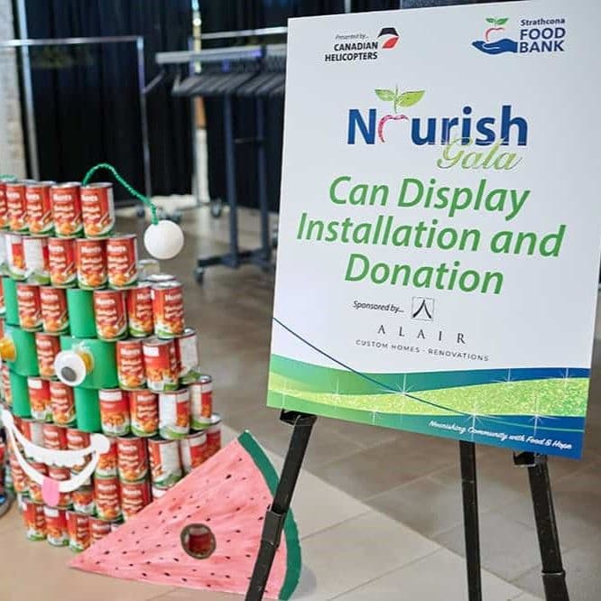 Photo shows cans of food stacked high as a form of art showing a face and a watermelon slice.
