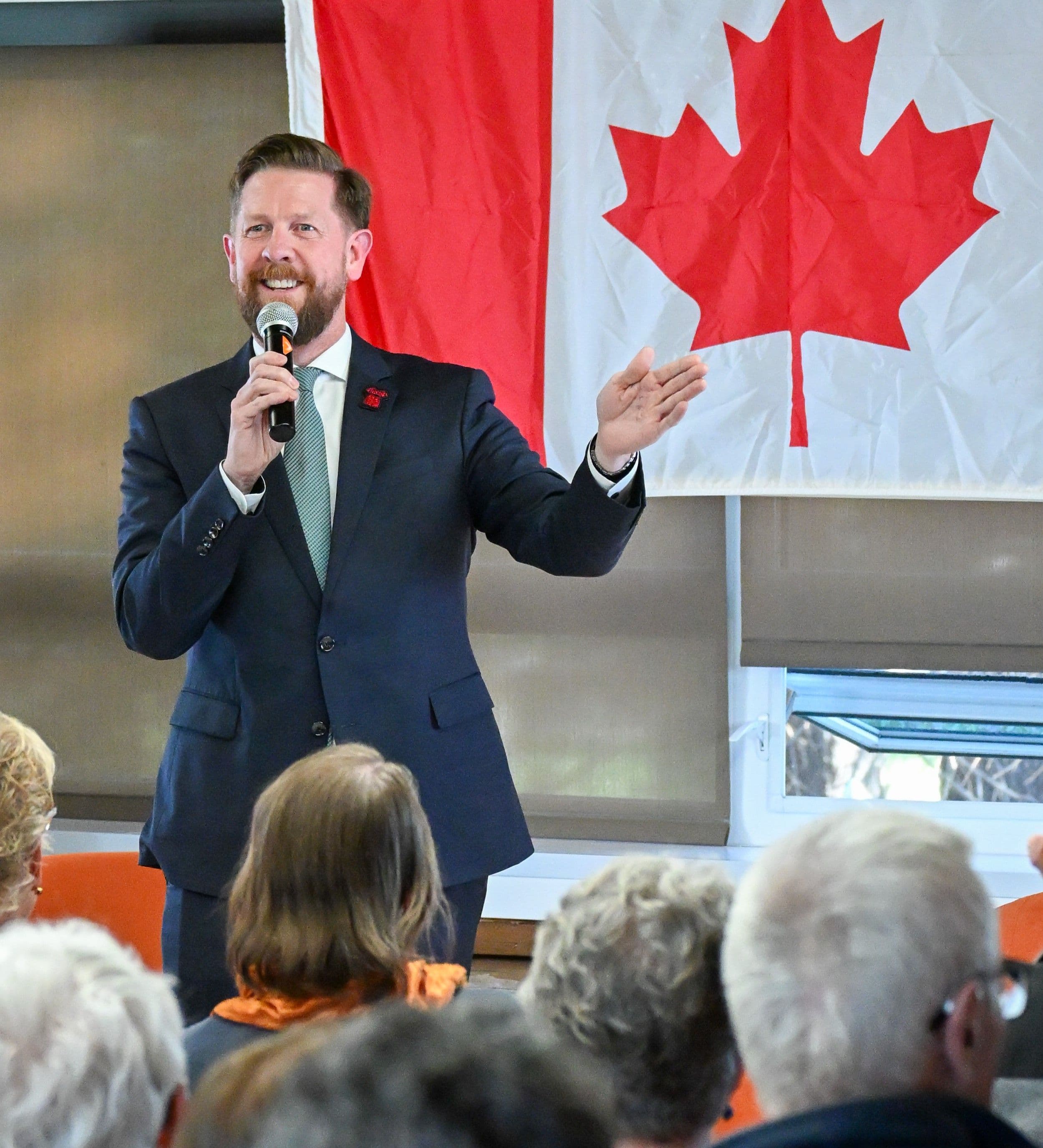 Kyle Kasawski stands in front of a Canada flag holding a microphone.
